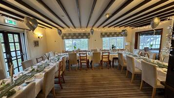 A dining area with tables set for a meal, featuring striped ceiling beams and large windows.