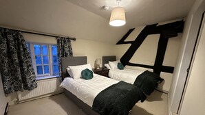 A bedroom with two beds, a window with curtains, a lamp, and a ceiling light. - The White Horse Inn (Shrewsbury)
