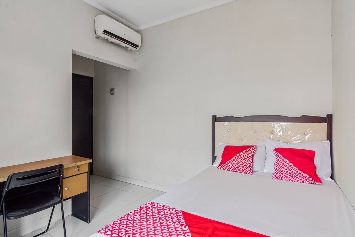 A bedroom with a bed, a desk, and an air conditioning unit.