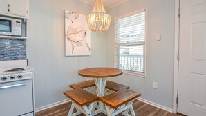 A kitchen with a white stove, a wooden table with benches, a chandelier, and a window with blinds.