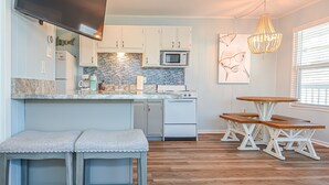 A modern kitchen with white cabinets, a tiled backsplash, and a wooden dining table with benches.