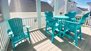 A covered outdoor area with a table and chairs, a white railing, and a view of houses in the background. - Pebble Beach East Home with Bay Creek Amenities (Cape Charles)