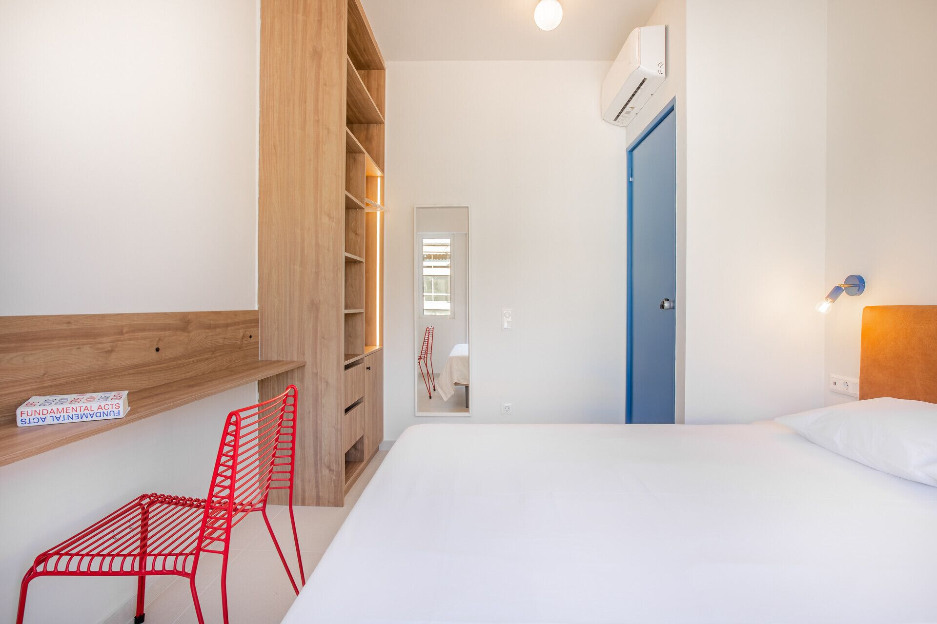 Une chambre à coucher avec un lit, une armoire en bois, une chaise rouge et une porte bleue.