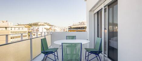 A balcony with a table and chairs, a view of buildings, and a large window.