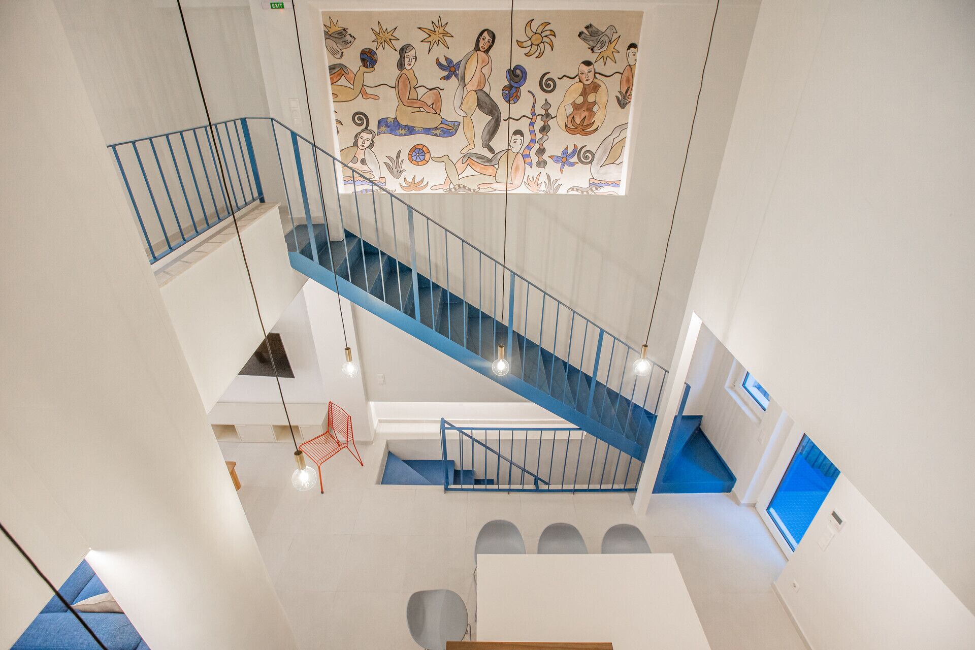 Un interior de varios niveles con una escalera azul, un mural y una silla roja.