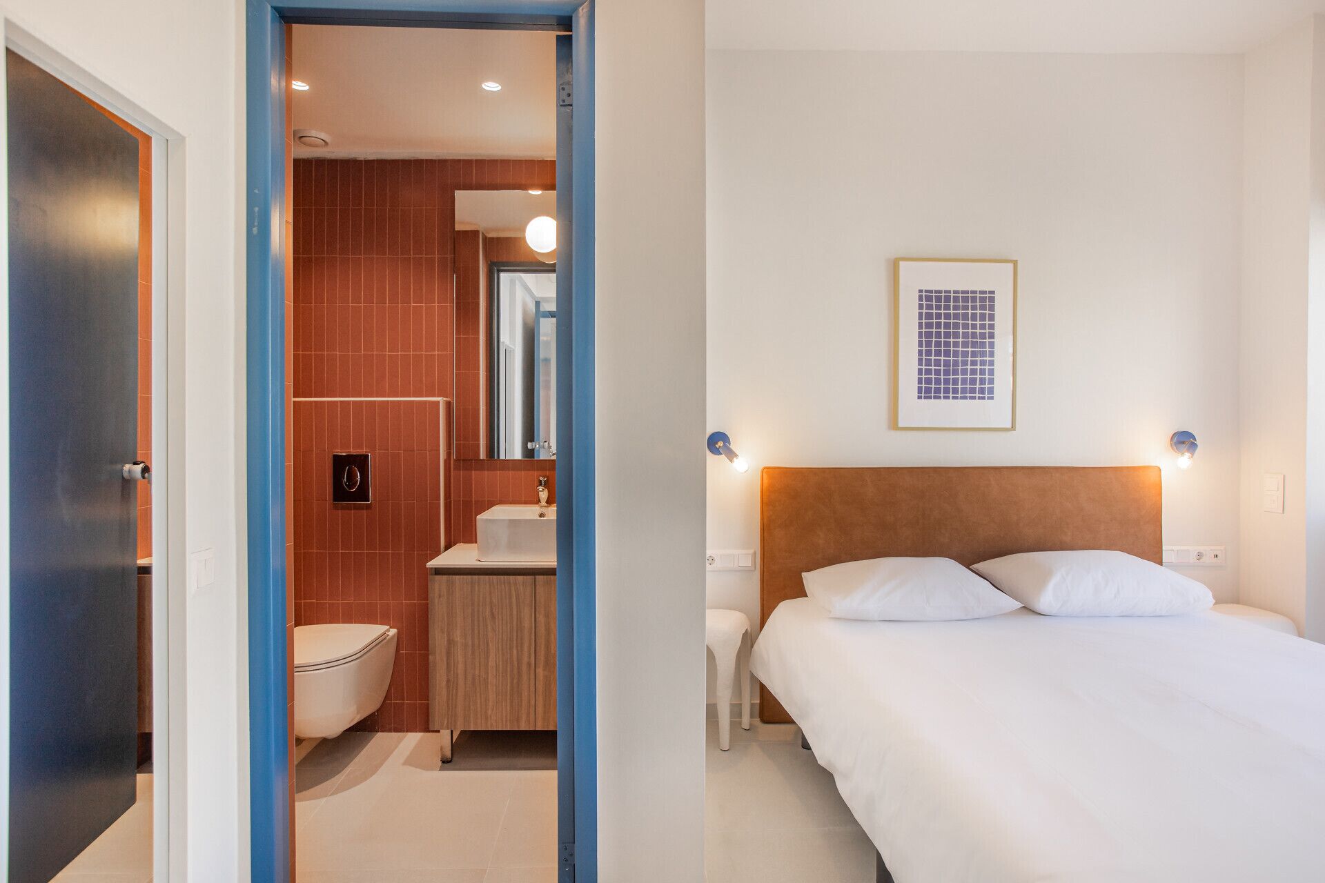 Habitación de hotel con cama, mesita de noche y baño completo con inodoro, lavamanos y espejo.