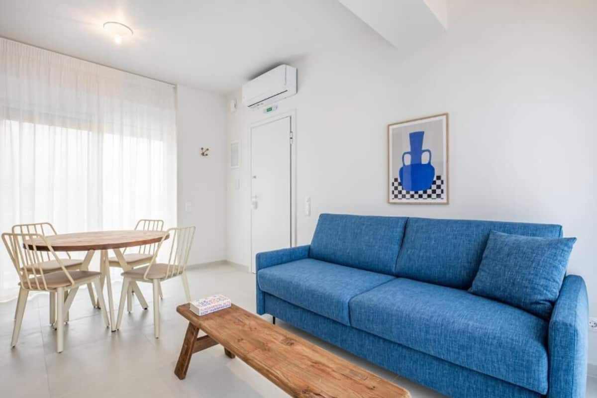 A room with a blue sofa, a wooden table, and a dining table with chairs.