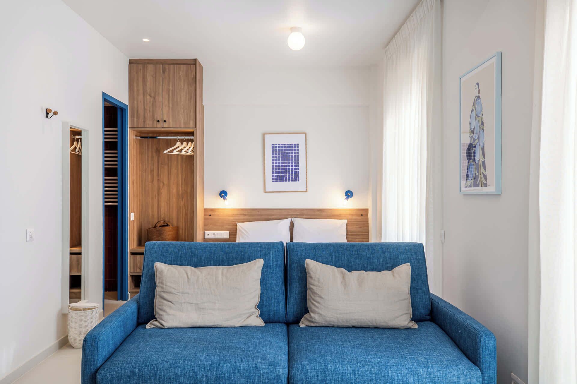 A room with a blue sofa, wooden wardrobe, and a bed with a headboard.