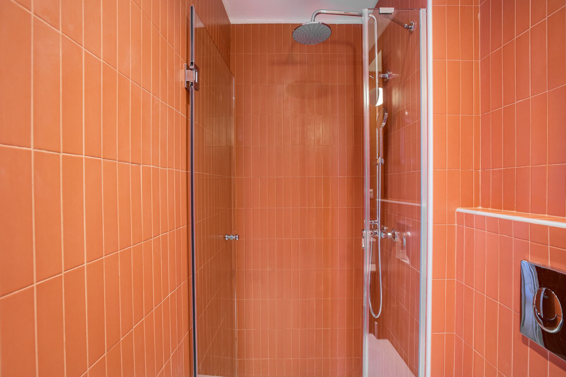 Ducha con puerta de vidrio, cabezal de ducha manual y panel de control en la pared.