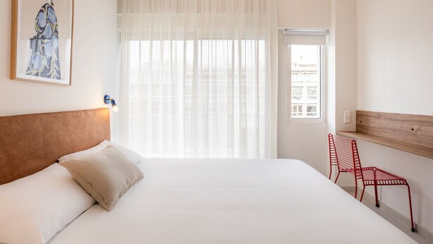 A hotel room with a bed, a window with sheer curtains, a red chair, and a framed picture on the wall. - Kallithea Apartments by Olala Homes (Kallithea)