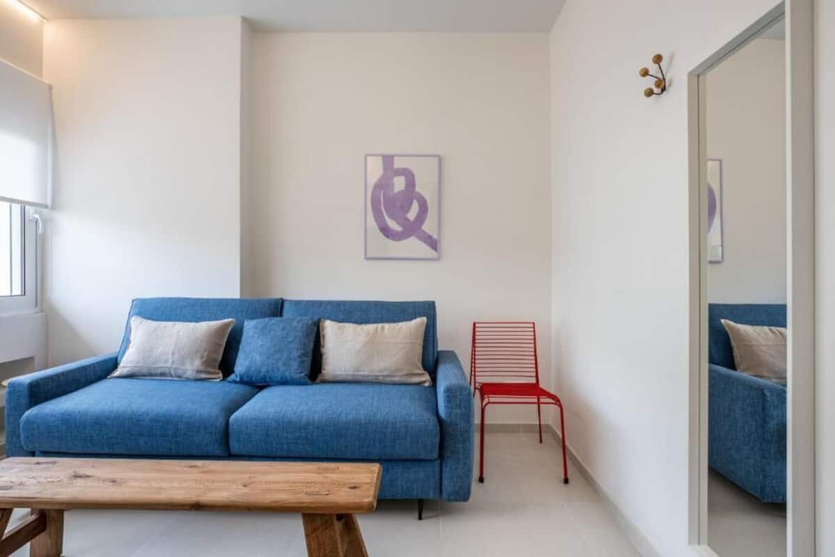 A modern living room with a blue sofa, a wooden coffee table, and a red chair.