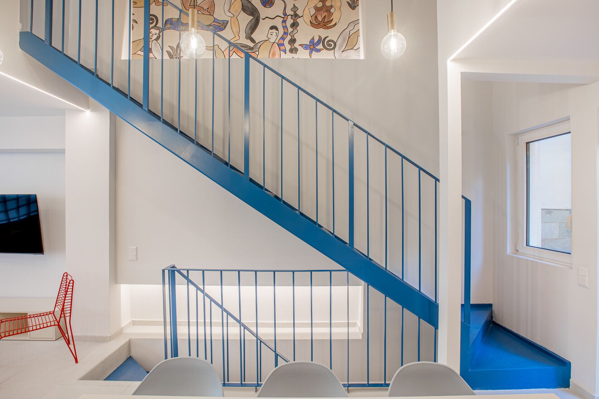 Una escalera con barandas azules, una lámpara de pared y un ventanal.