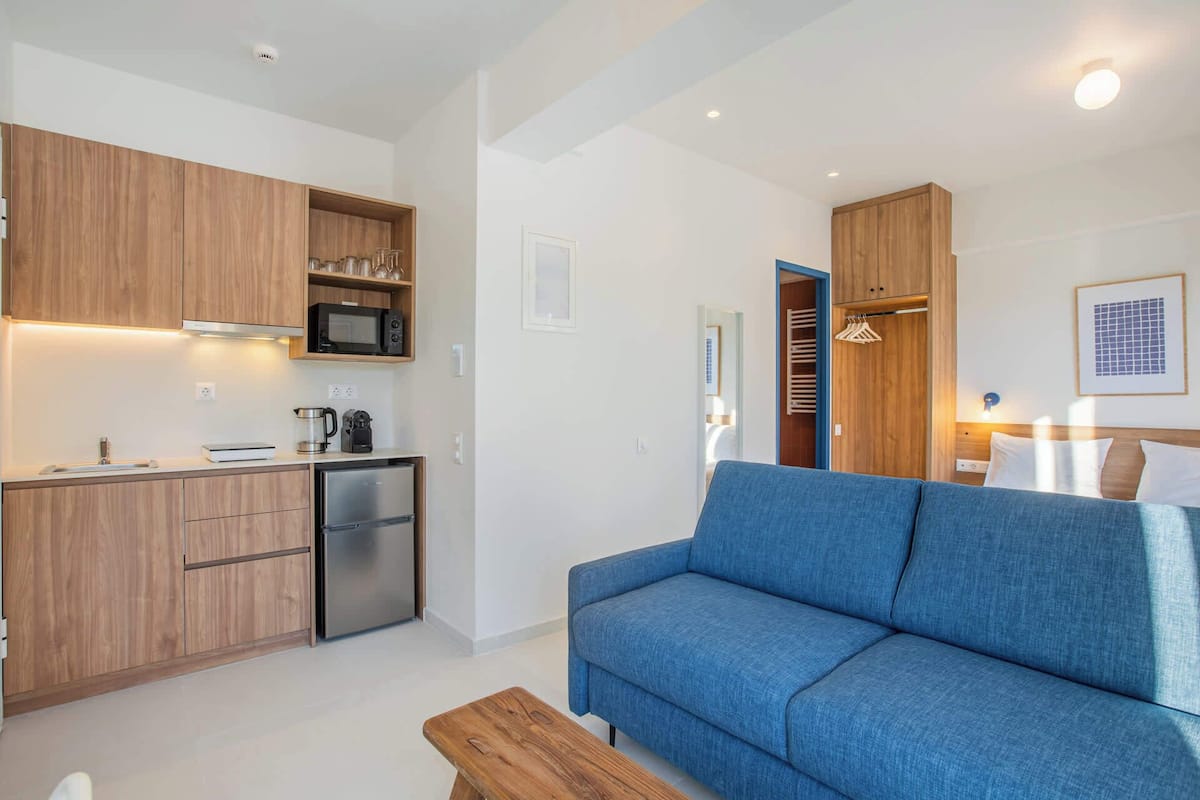 A compact living space with a kitchenette, a sofa, and a wooden bench.