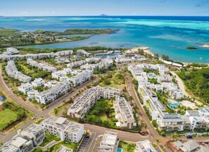 An aerial view of a coastal residential area with modern buildings, roads, and a beach. - Appartement Cosy Près de la Plage Dans la Résidence Resort Renomée D'azuri (ROCHES NOIRES)