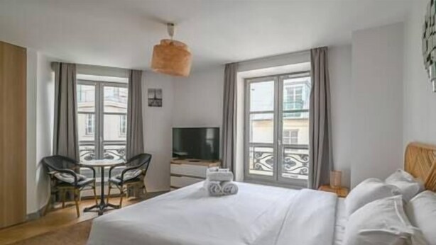 Ett hotellrum med en säng, ett skrivbord, en stol, en tv och stora fönster.