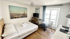 A hotel room with a bed, a desk, a chair, a TV, and a window with a view of a cityscape.