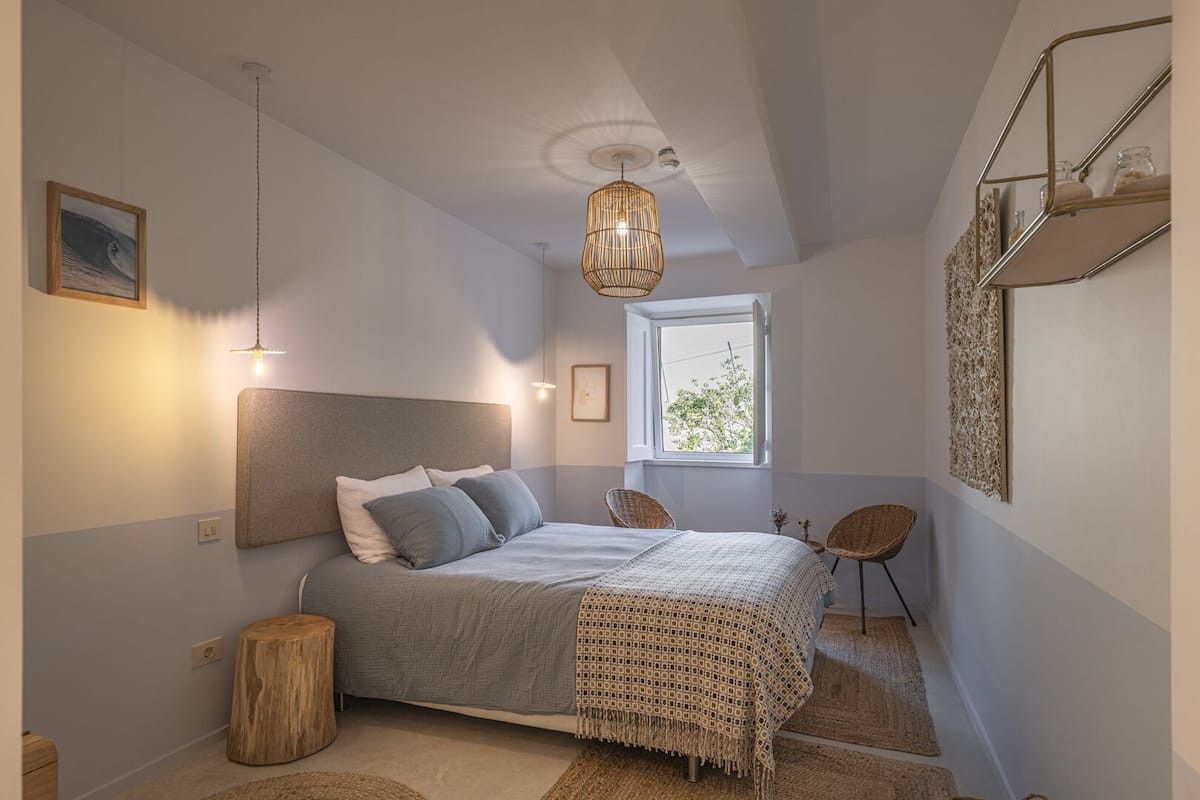 A bedroom with a bed, bedside tables, a window, and a hanging light fixture.