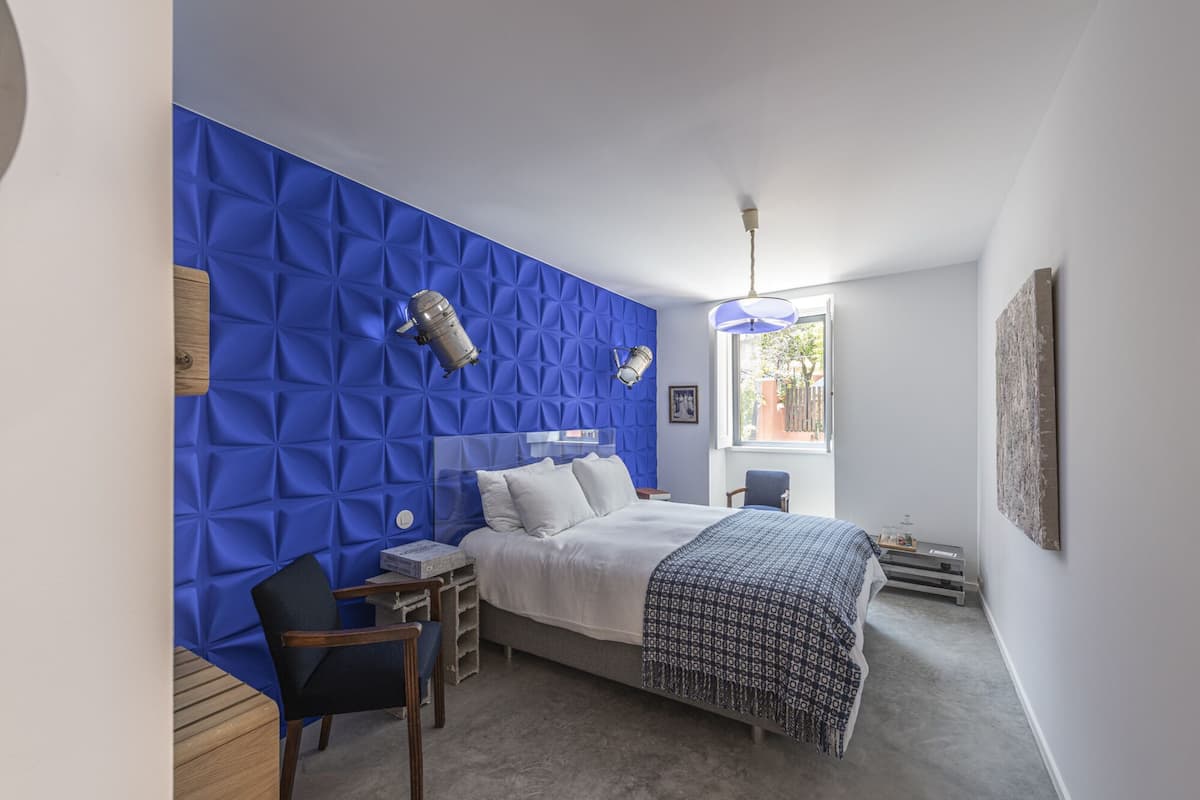 A bedroom with a blue textured wall, a bed with white bedding, a wooden chair, and a small table.