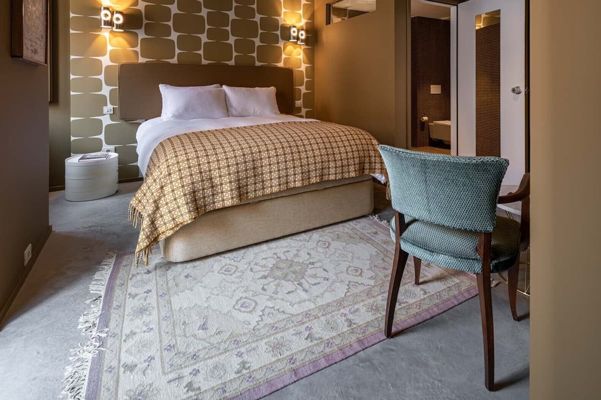 A bedroom with a bed, bedside lamps, a chair, and a patterned rug.
