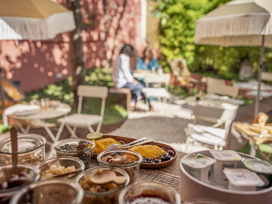 An outdoor dining area with tables and chairs, a variety of food and drink containers, and umbrellas providing shade.