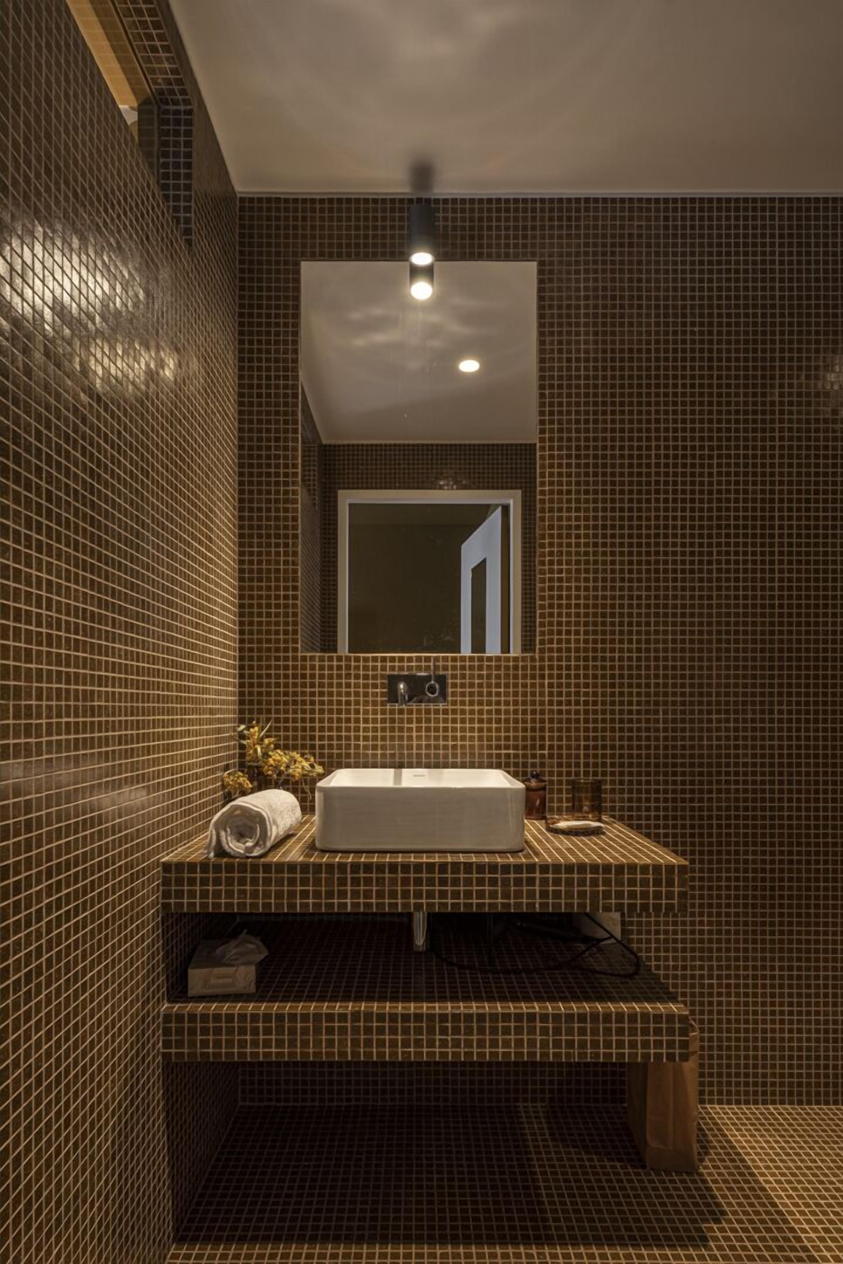 Un baño con pared de azulejos, un lavamanos, un espejo y un perchero para toallas.