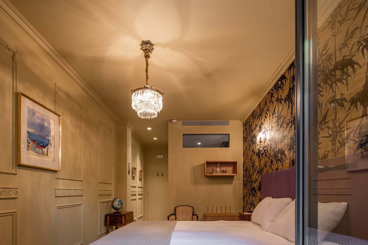 A hotel room with a large bed, a chandelier, a globe on a side table, and a painting on the wall.