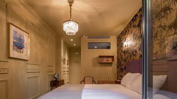 Habitación de hotel con una cama grande, un candelabro, un globo terráqueo sobre una mesita auxiliar y un cuadro en la pared.