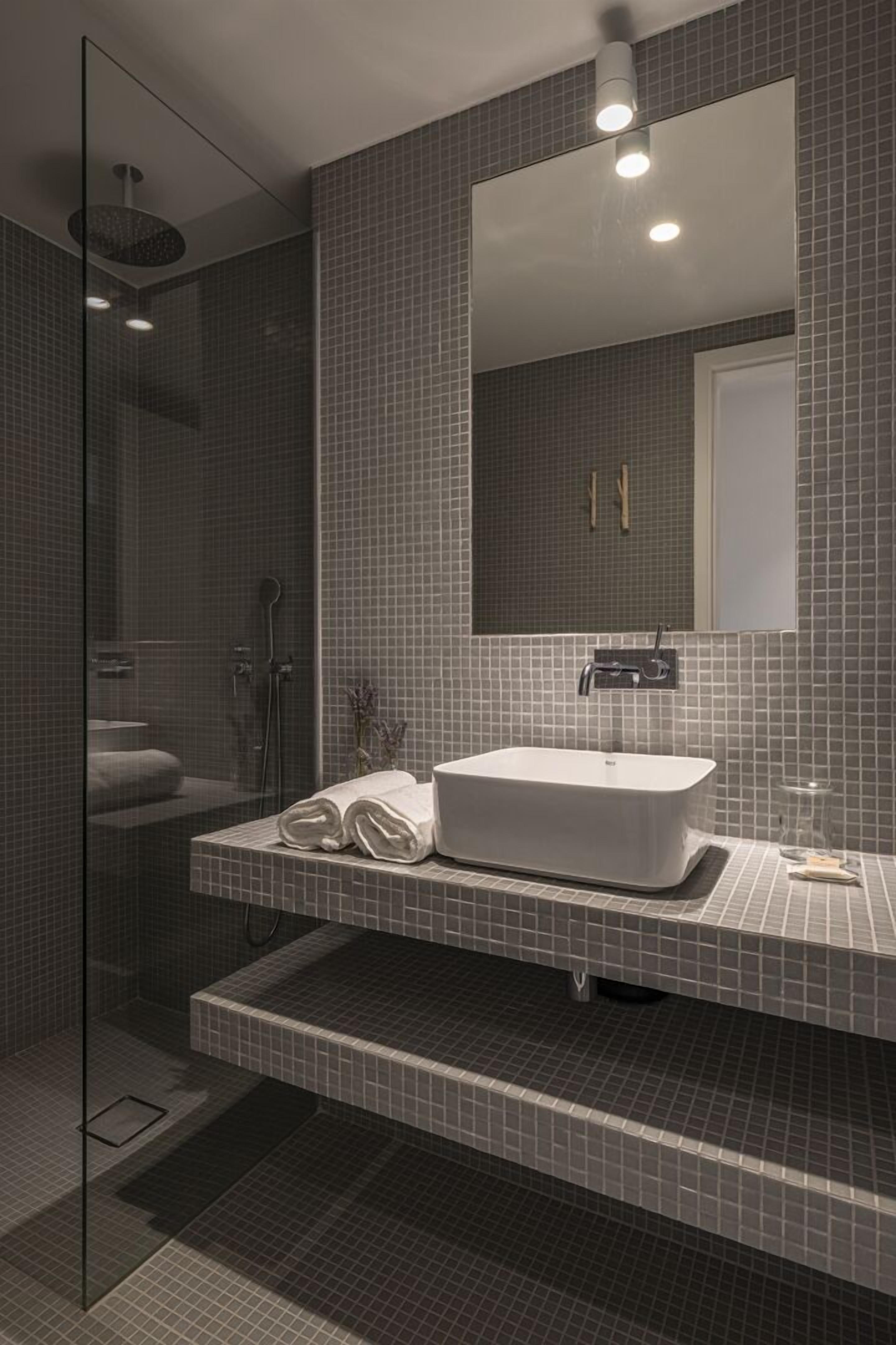 Un baño moderno con ducha de vidrio, lavamanos blanco y un espejo grande.