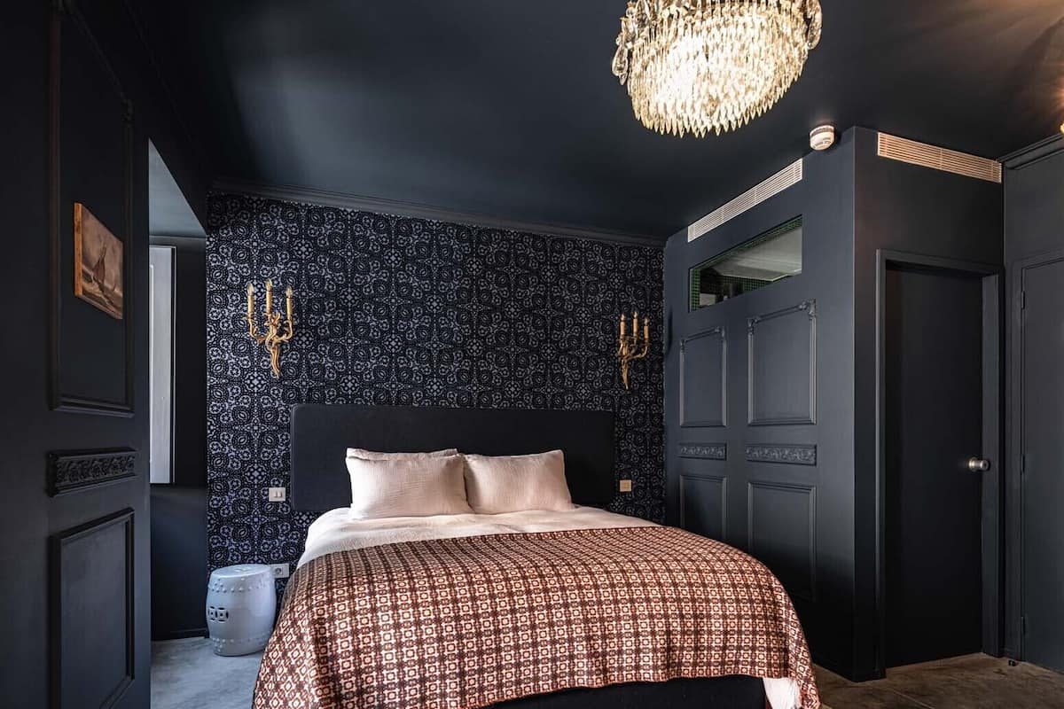 A bedroom with a large bed, a chandelier, a patterned wall, and a door.