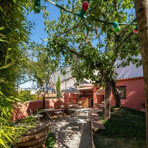 An outdoor patio area with tables and chairs, surrounded by greenery and a building with a red facade. - toctoctocLisboa (Lisbon)