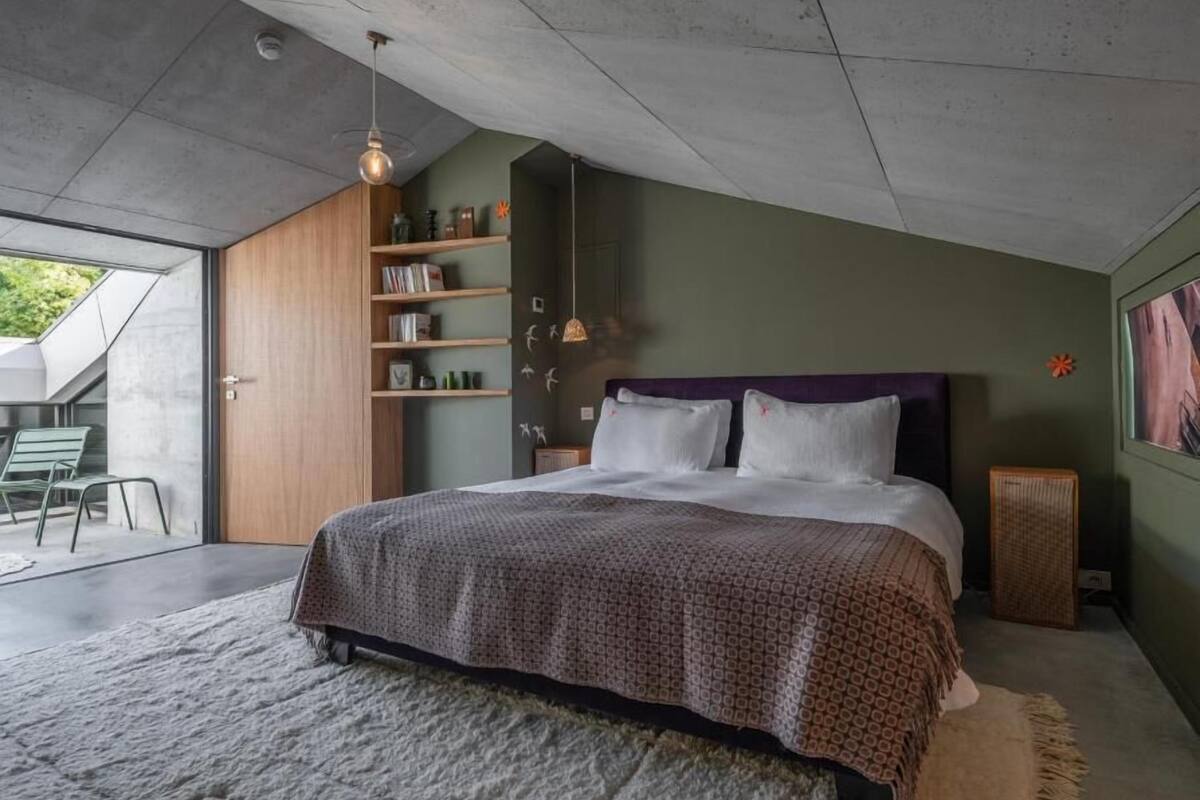A modern bedroom with a large bed, a wooden wardrobe, a built-in bookshelf, and a large window.