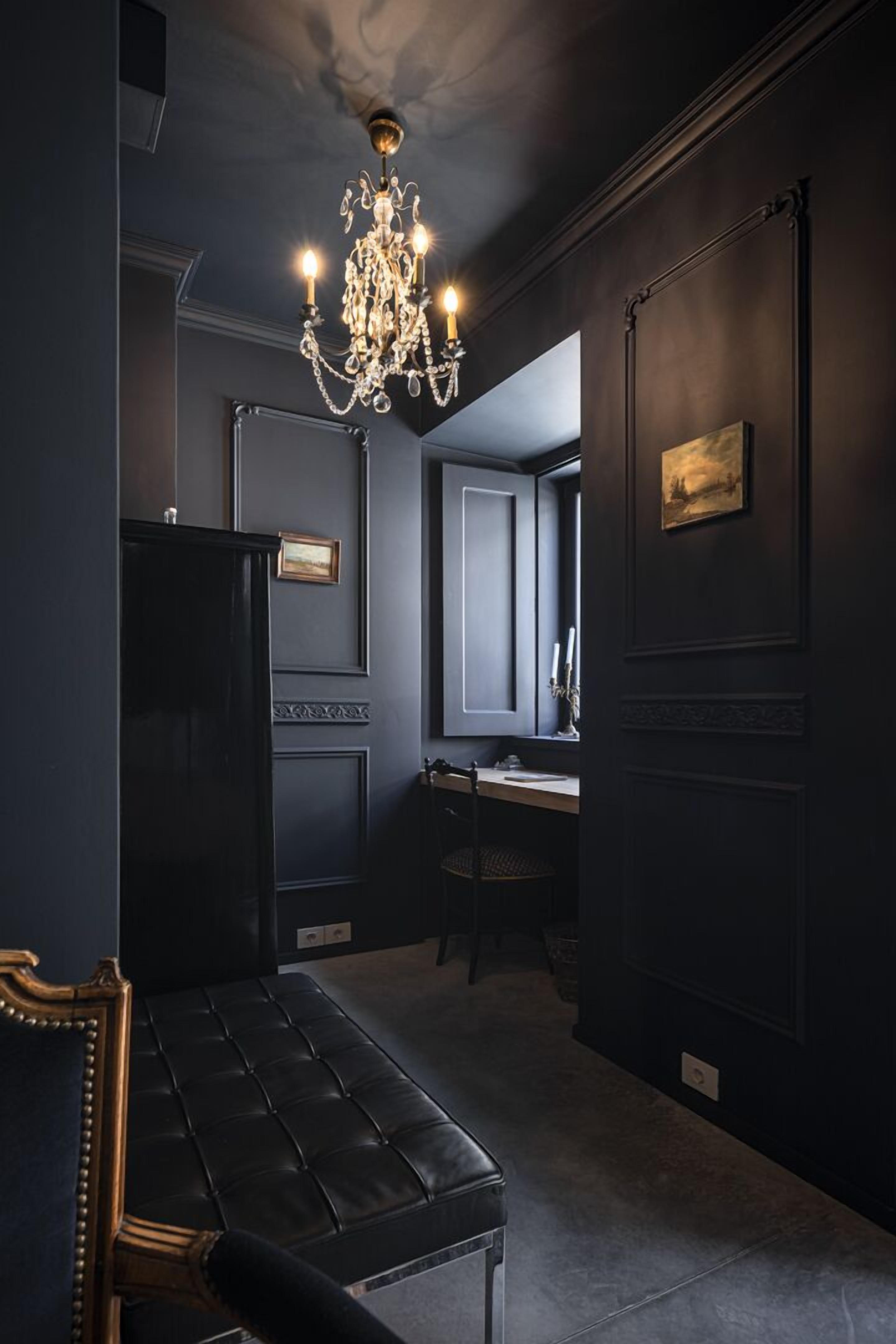 Une pièce aux couleurs sombres, agrémentée d’un lustre, d’un banc et d’un bureau avec une chaise.