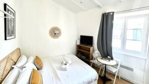 A bedroom with a bed, a TV, a chair, and a window with curtains. - Magnifique appartement à Opéra (Opéra6D) (Paris)