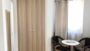 A room with a wooden wardrobe, a round table with chairs, and a window with curtains.