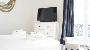 Ein Hotelzimmer mit einem Bett, einem Fernseher auf einer Kommode, einem Sessel und einem Fenster mit Vorhängen.