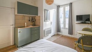 Une petite chambre comprenant un lit, une kitchenette et un téléviseur.