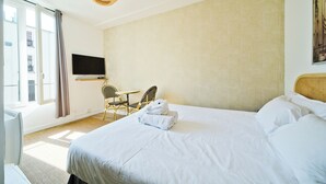 Une chambre d’hôtel avec un grand lit, un téléviseur à écran plat, une petite table, deux chaises et une grande fenêtre.