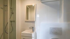 A bathroom with a glass shower enclosure, a white sink with a mirror above it, and a toilet with a flush button. - So cute typical french apartment (Paris)