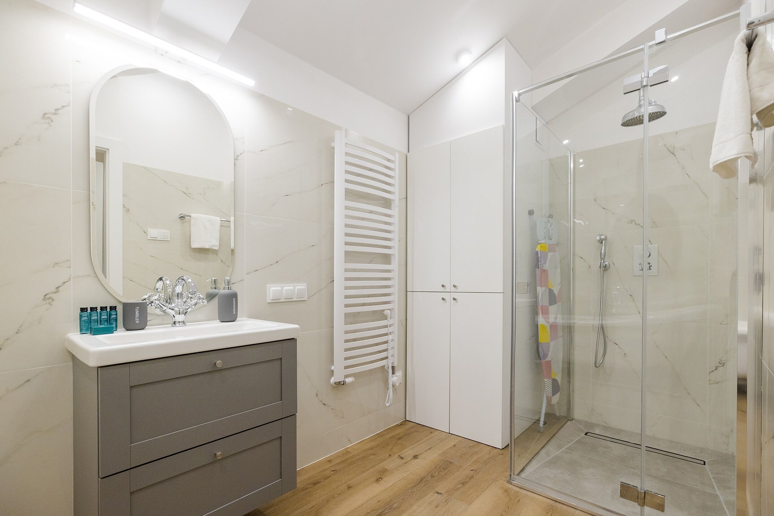 A modern bathroom with a marble vanity, a glass shower enclosure, and a white towel hanging on the wall.
