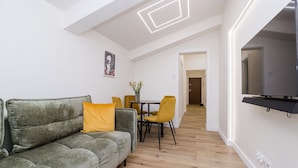 A modern living room with a grey sofa, yellow cushions, a dining table with yellow chairs, and a flat-screen TV mounted on the wall. - ShortStayPoland Zelazna B146 (Warsaw)