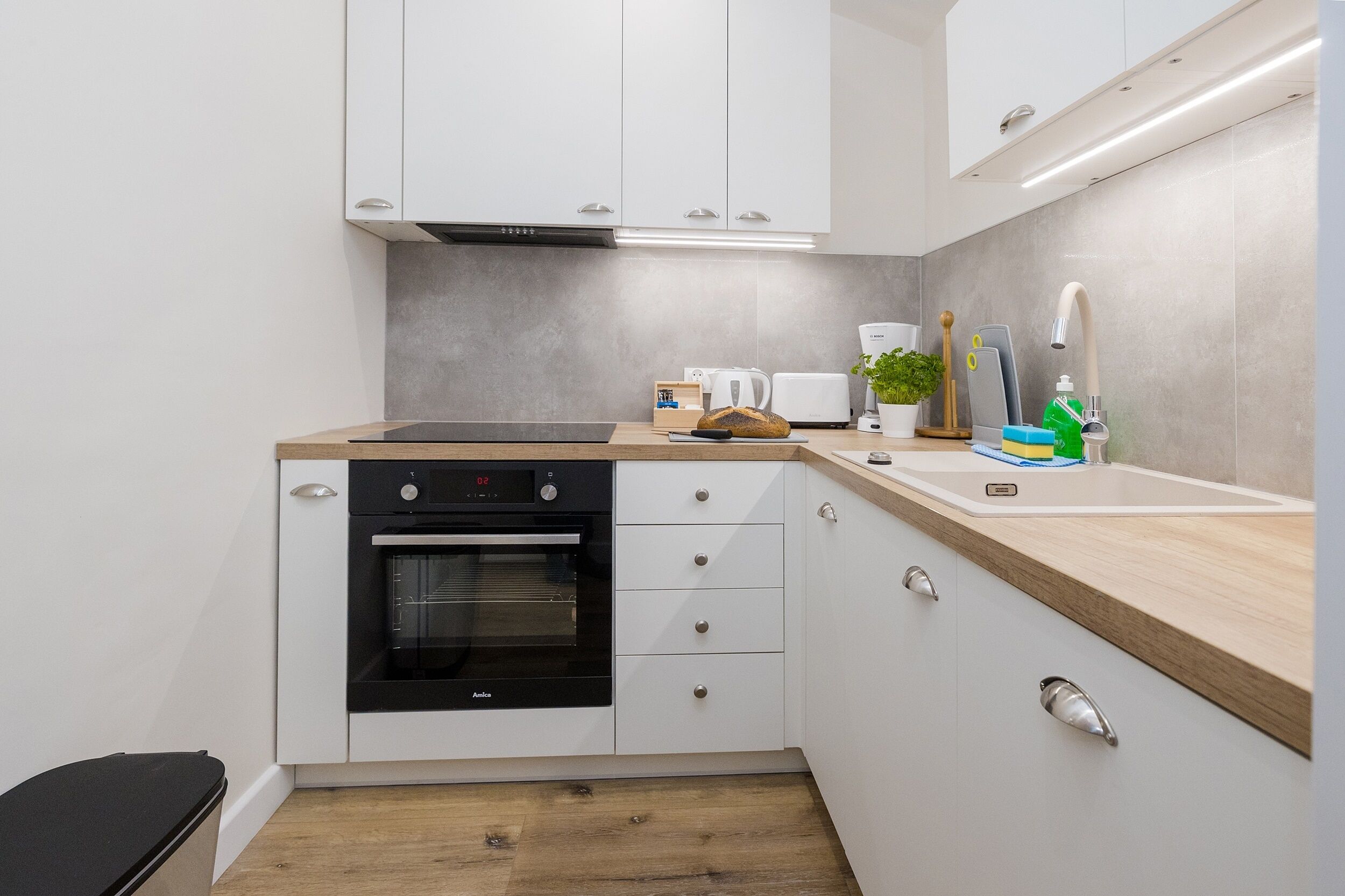 Una cocina moderna con armarios blancos, un horno negro, una encimera de madera, un fregadero y una cafetera.