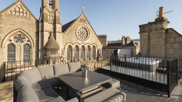 Una terraza en la azotea con un área de estar exterior moderna, vistas a una iglesia histórica y un cielo despejado.