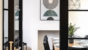 Un comedor moderno con una mesa de madera y sillas negras, una lámpara colgante negra y una obra de arte abstracta montada en la pared.