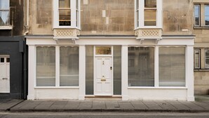 Un edificio con fachada blanca, dos ventanas con contraventanas y una puerta con un letrero encima.