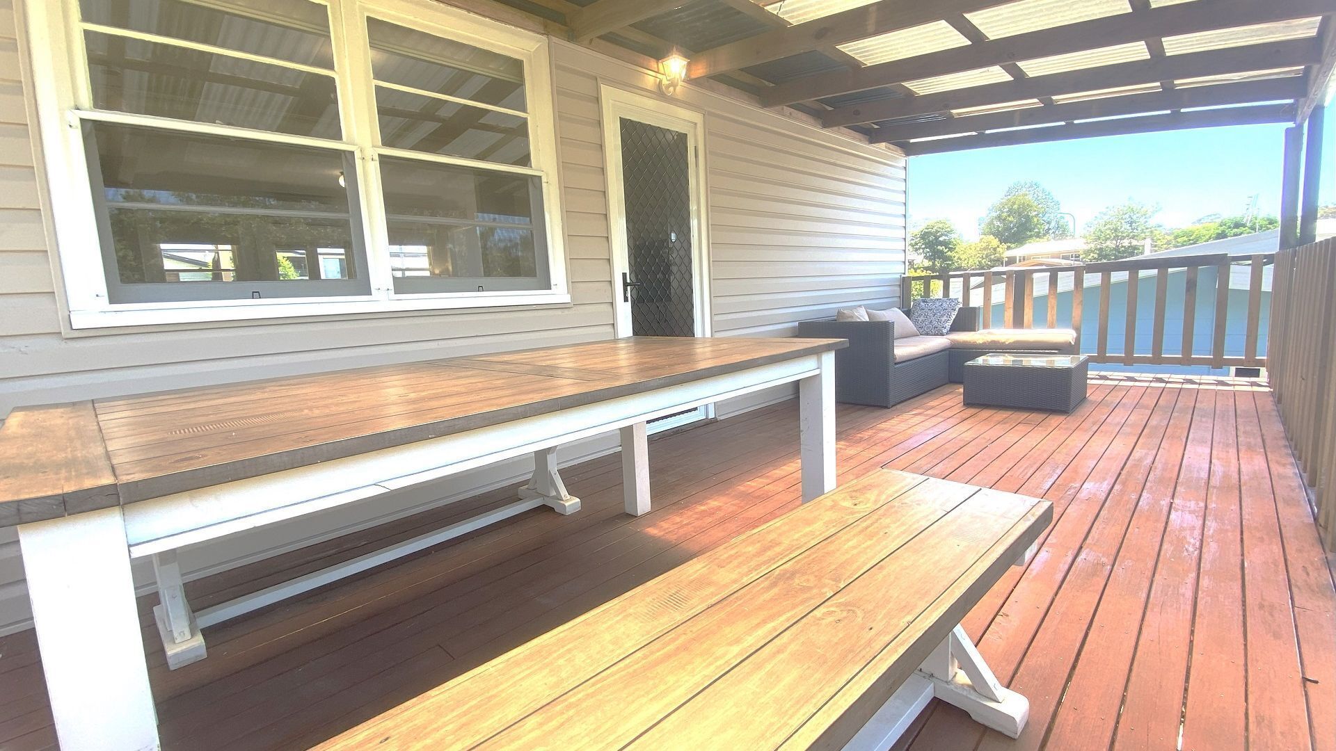 An outdoor deck with a wooden bench and a sofa, a covered area with a pergola, and a view of the surrounding landscape.