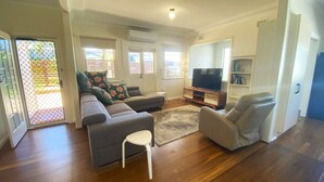 Una sala de estar con un sofá gris, una silla blanca, un mueble para televisor y una estantería.