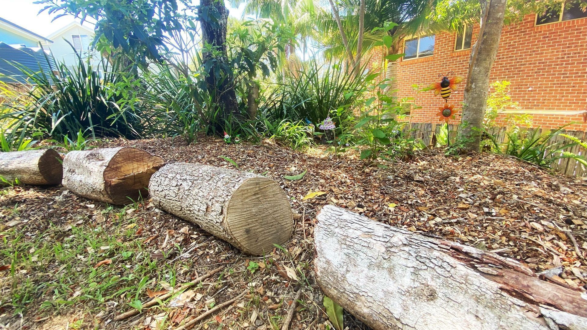 Un jardín con troncos, un edificio de ladrillo y diversas plantas.