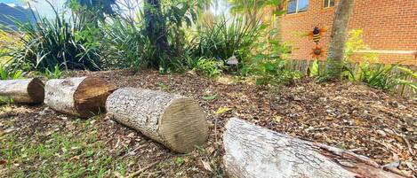 Un jardín con troncos, un edificio de ladrillo y diversas plantas.