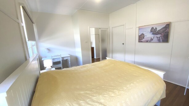 Un dormitorio con cama, escritorio y silla. Hay una puerta y un cuadro en la pared.