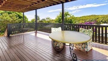 An outdoor wooden deck with a table and chairs, surrounded by a wooden fence and lush greenery.